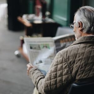 Elderly man reading a newspaper in an outdoor cafe setting, enjoying a peaceful moment.