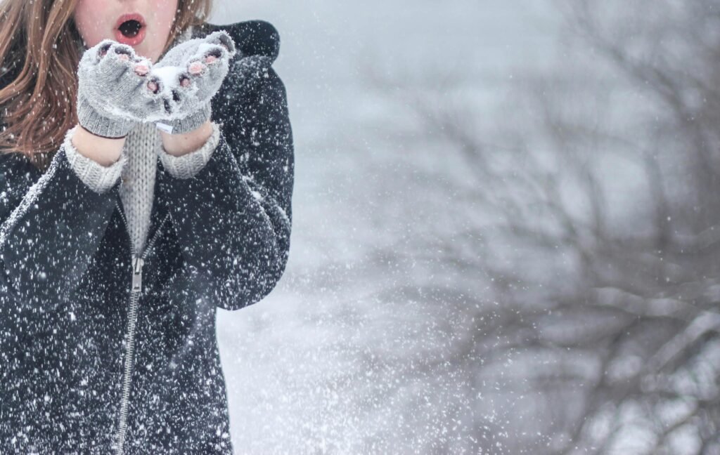 pexels-photo-54200-54200 Woman in cozy winter clothing blowing snowflakes with excitement outdoors in a snowy setting.