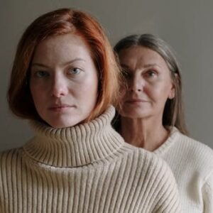 A serene portrait of a mother and daughter in cozy sweaters against a gray background.